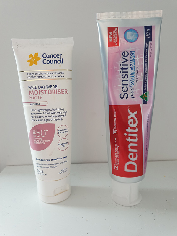 A tube of sunscreen near a tub of toothpaste. They are similar in size and color.